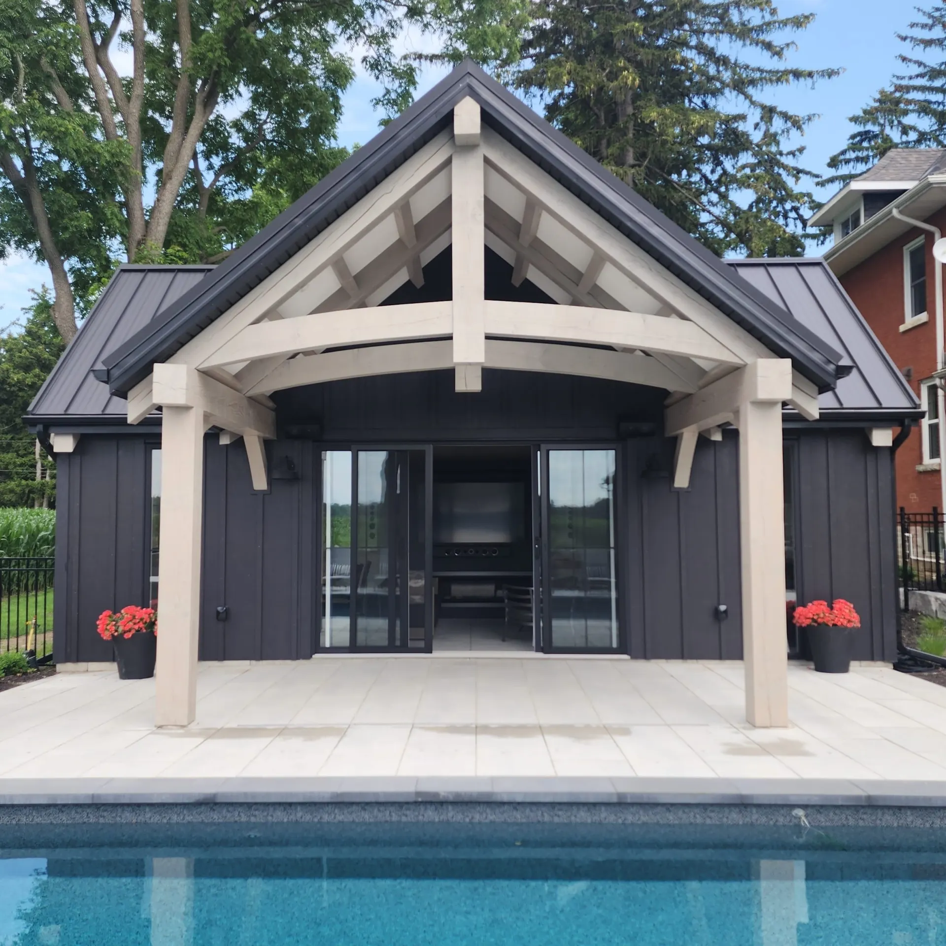 Dark pool house with exposed timber frame beside a pool